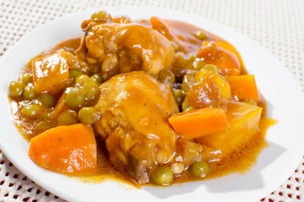 Prato branco com ensopado de frango com batata, cenoura e ervilhas